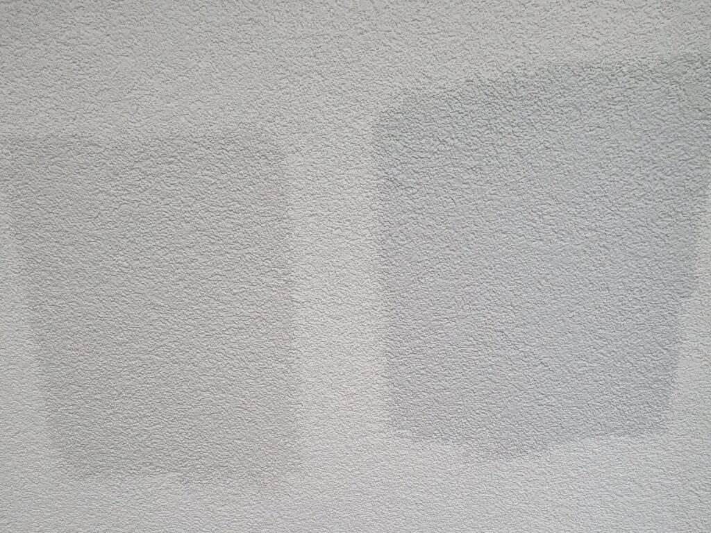 Zwei nebeneinander aufgetragene Farbmuster auf verputzter Wand, links ein wärmeres Hellgrau, rechts ein kühleres Mittelgrau, auf rauer Putzstruktur.