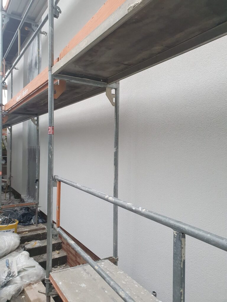 Frisch gestrichene Hausfassade mit abgedecktem Boden und noch stehendem Gerüst nach Abschluss der Malerarbeiten.